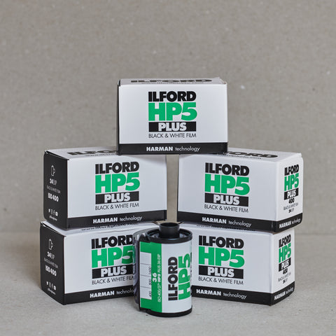 Ilford HP5 Plus black and white film boxes and a roll of film on a gray background